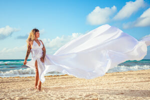 joven tatuada con vestido volador blanco en la playa de cancun
